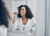 woman in a white bathrobe brushing her teeth